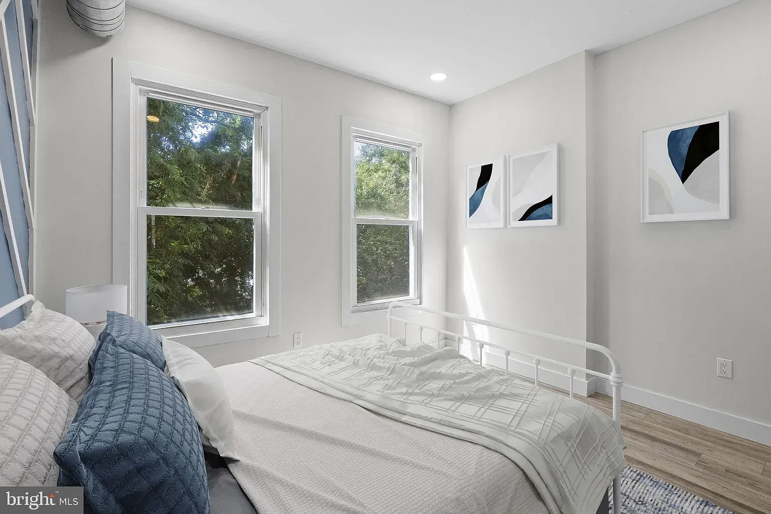 Furnished Unit B bedroom with white bedding, blue pillows, and two windows