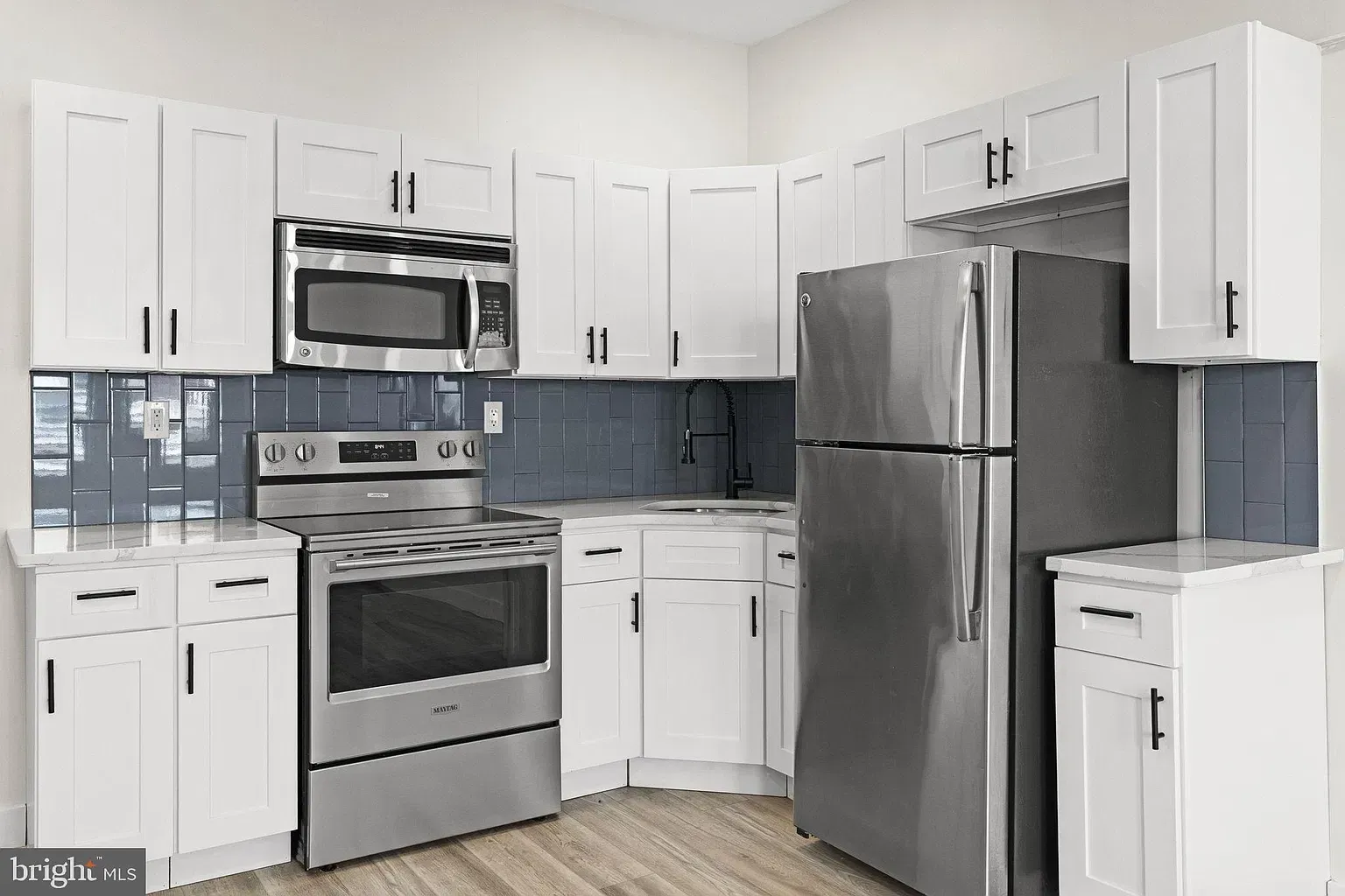 Unit B kitchen with white cabinetry, stainless steel appliances, and blue tile backsplash