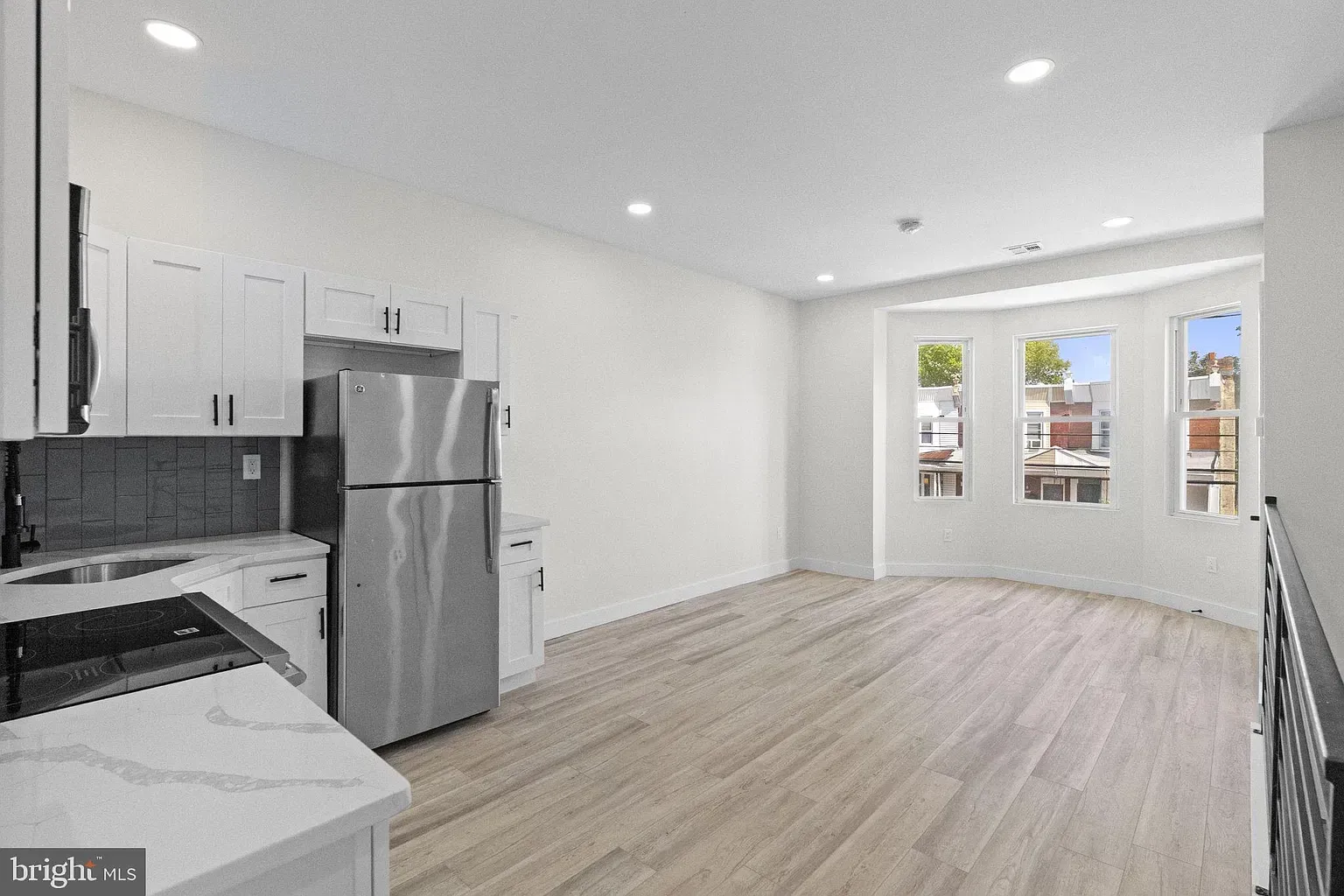 Unit B kitchen and living area with white cabinetry, stainless appliances, and wood-look floor