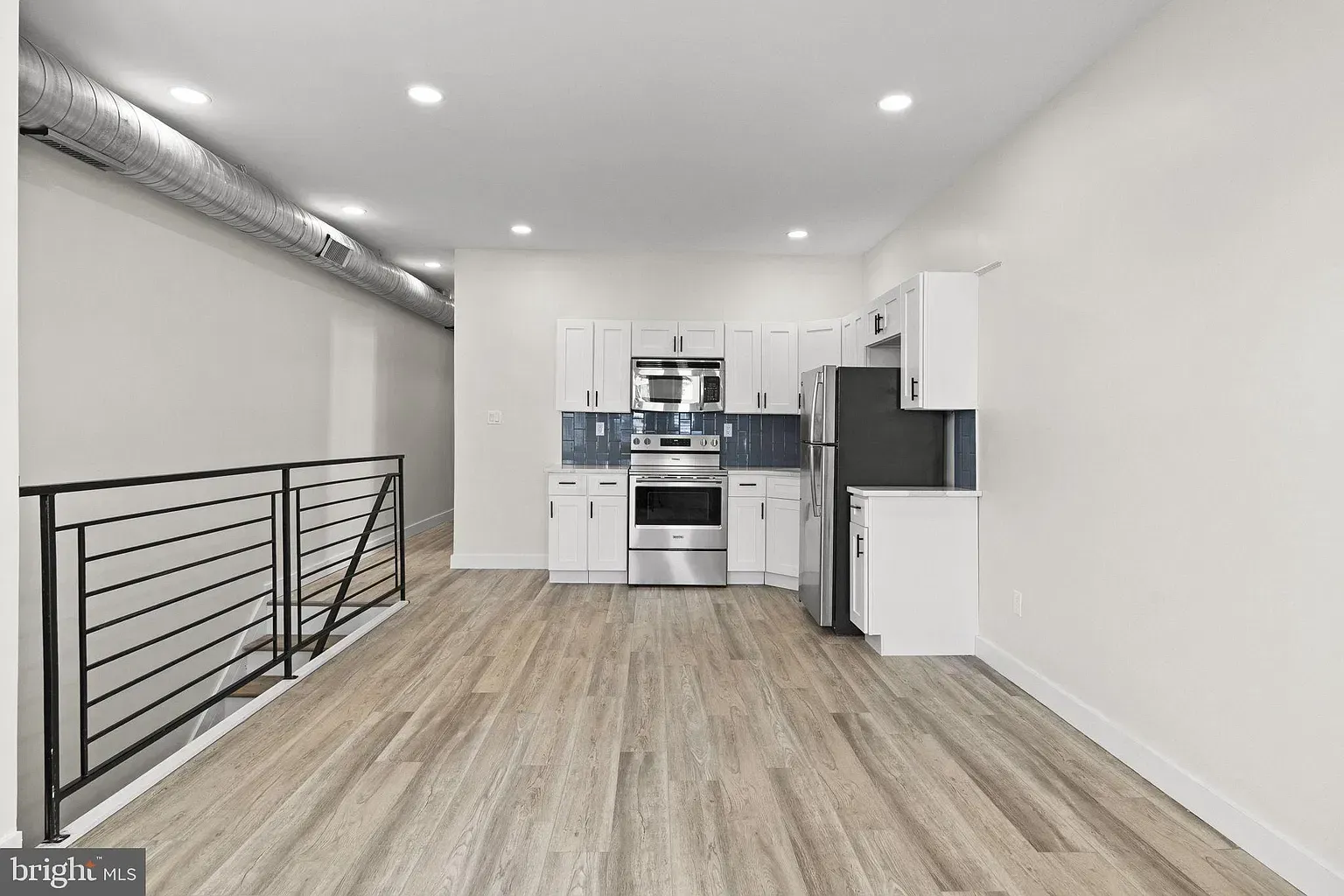 Unit B open living and kitchen area with stainless steel appliances and blue tile backsplash